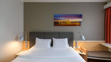 Ein Hotelzimmer mit einem Bett, zwei Nachttischlampen, einem Nachttisch, einem Schreibtisch und einem Stadtbild.