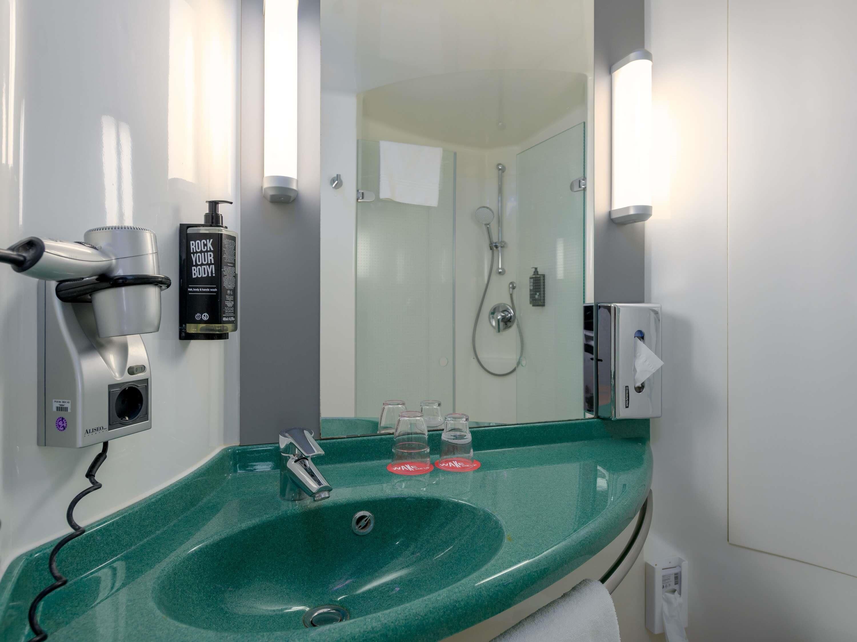 Een badkamer met een groene wastafel, een haardroger, een spiegel en een douche.