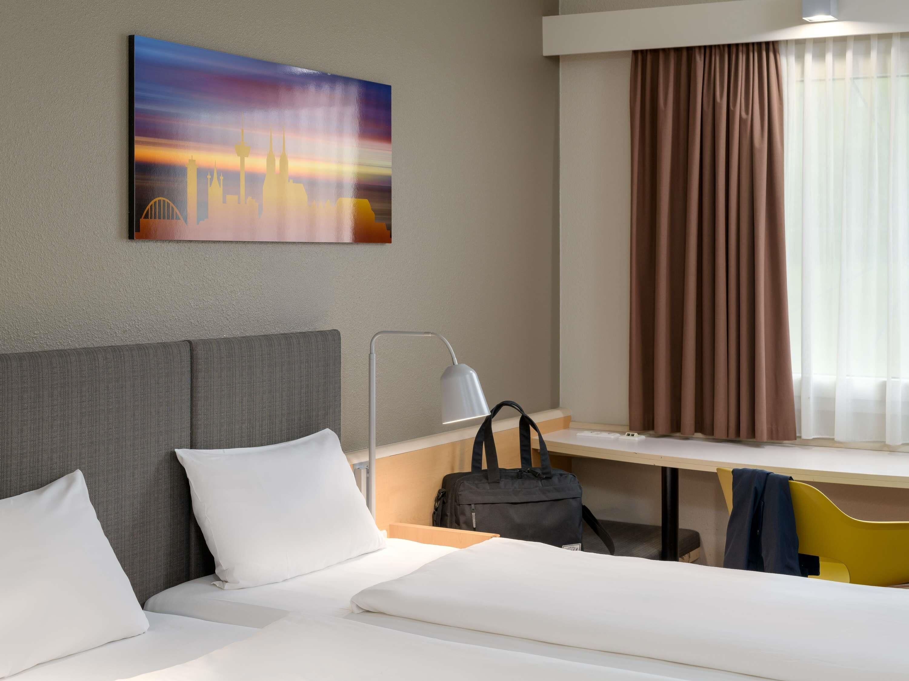 Une chambre d’hôtel avec un lit, un bureau, une chaise, une lampe et un tableau au mur.