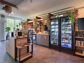 A modern bar area with a coffee machine, a beverage dispenser, and a refrigerator stocked with drinks.