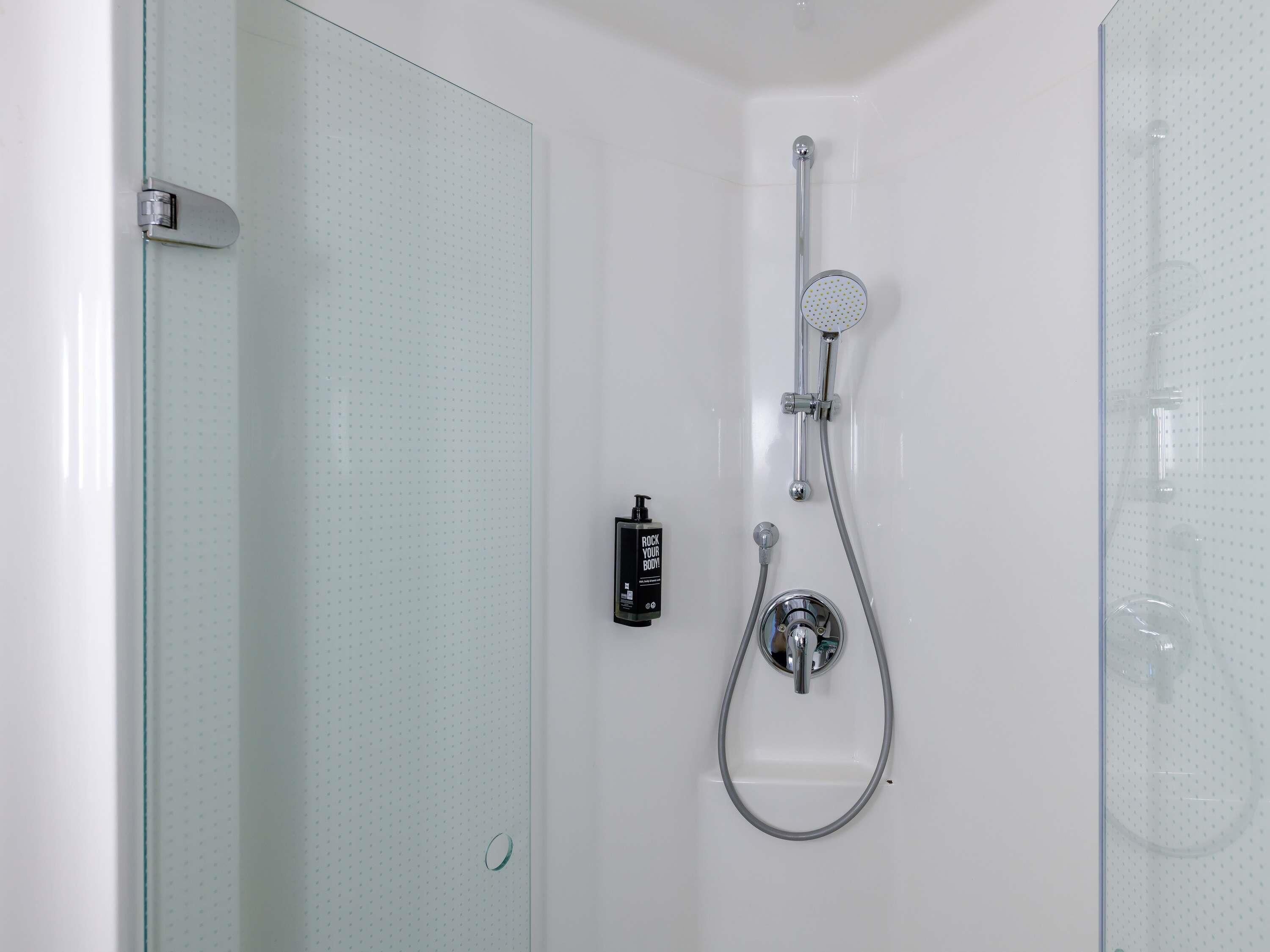 Une douche équipée d’un pommeau de douche à main, d’un robinet mural et d’un panneau de commande.