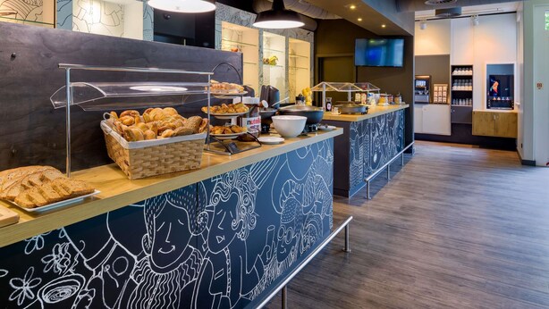 A buffet area with a variety of baked goods, a Nutella dispenser, and a television screen. - ibis Köln Airport (Cologne)