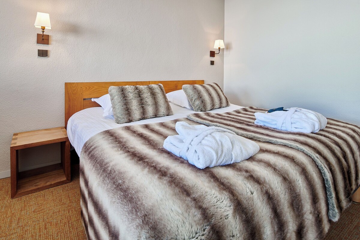 Une chambre d’hôtel avec un lit, deux oreillers, une table de chevet et une lampe fixée au mur.