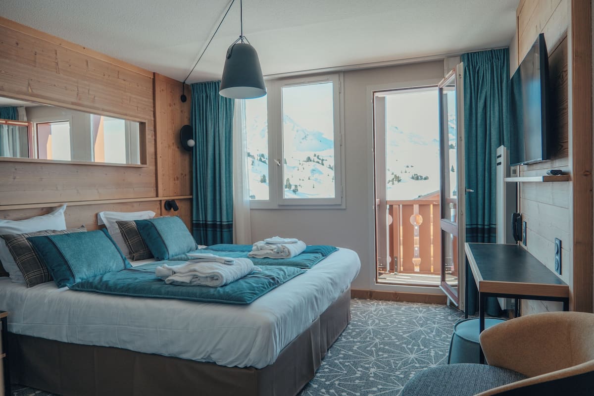 Ein Hotelzimmer mit Bett, Schreibtisch, Stuhl, Fernseher und einem Balkon mit Bergblick.