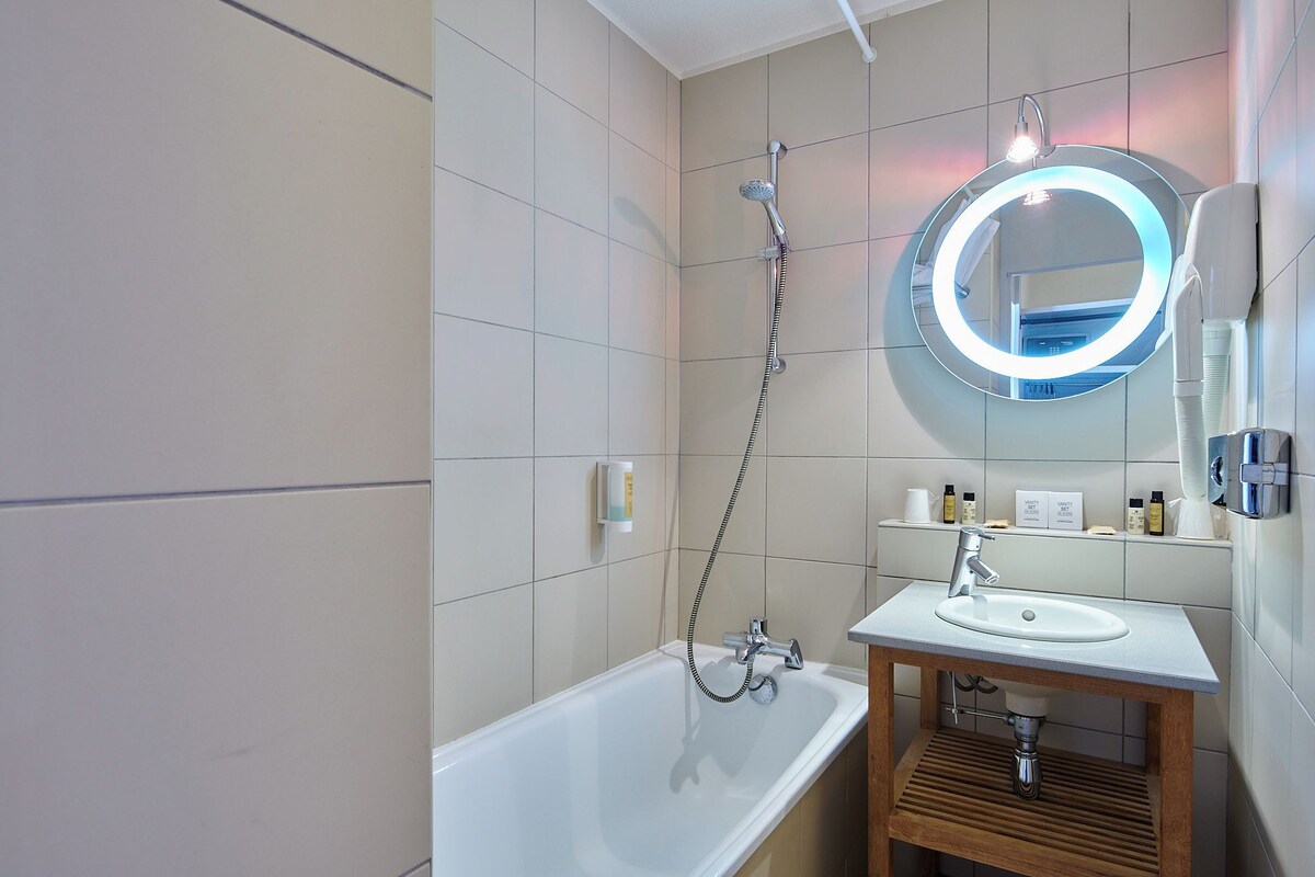 Une salle de bain moderne avec une baignoire, un meuble-lavabo avec un miroir et une pomme de douche.