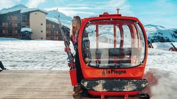 En röd linbana med namnet ”La Plagne Paradiski” står parkerad på en träplattform, med snötäckt mark och berg i bakgrunden.
