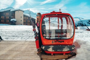 Une télécabine rouge portant l’inscription « La Plagne Paradiski » est garée sur une plateforme en bois, avec un sol enneigé et des montagnes en arrière-plan.