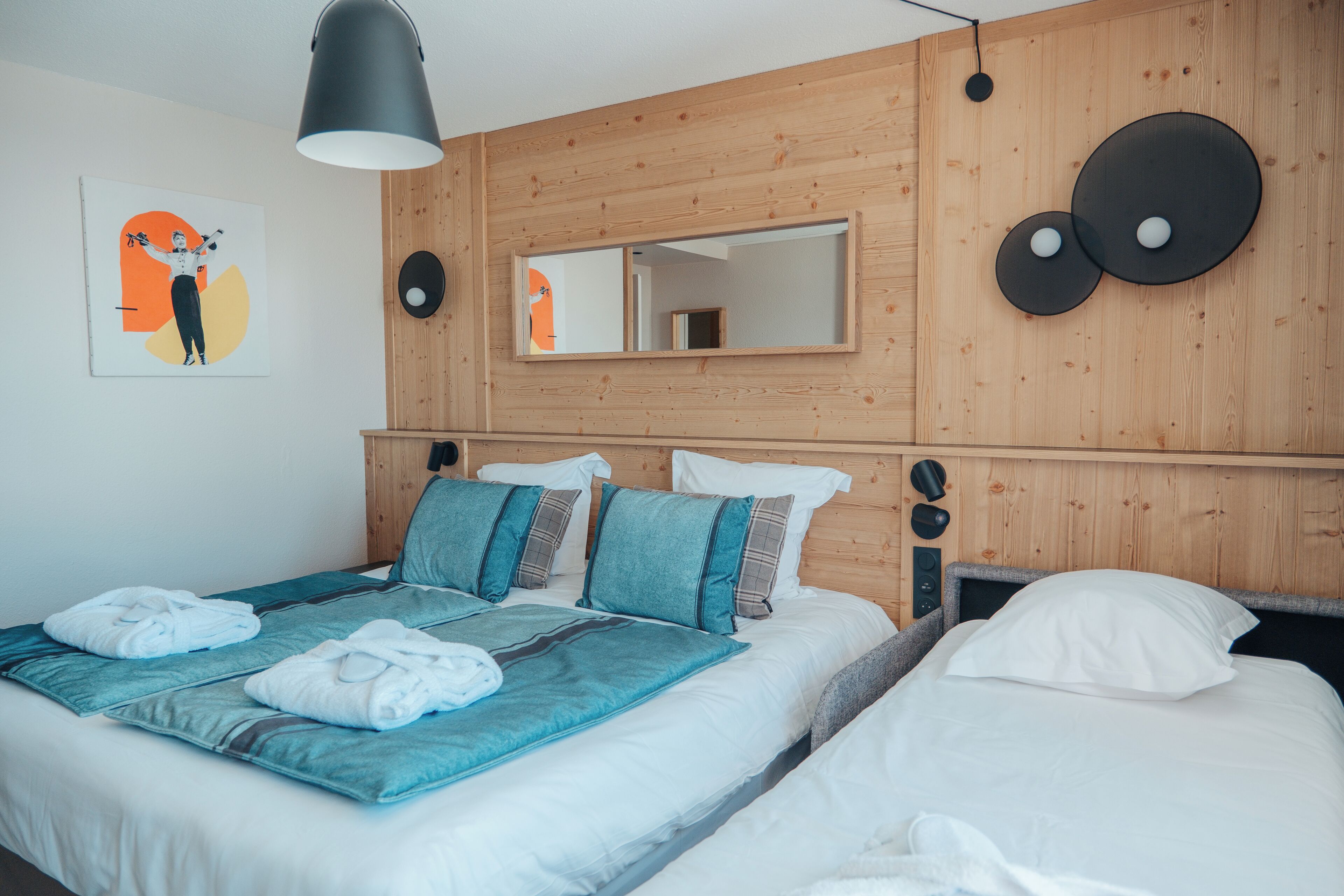 Una habitación de hotel con cabecera de madera, un espejo grande y una cama con ropa de cama azul y blanca.