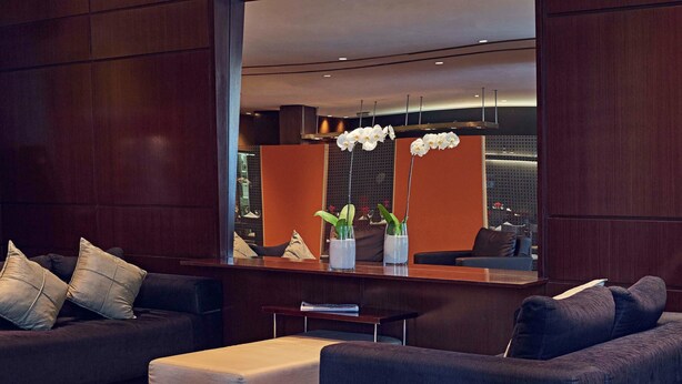 A modern lobby with dark sofas, a central ottoman, and a reception desk with a large mirror. - Mercure São Paulo Paulista Hotel (São Paulo)