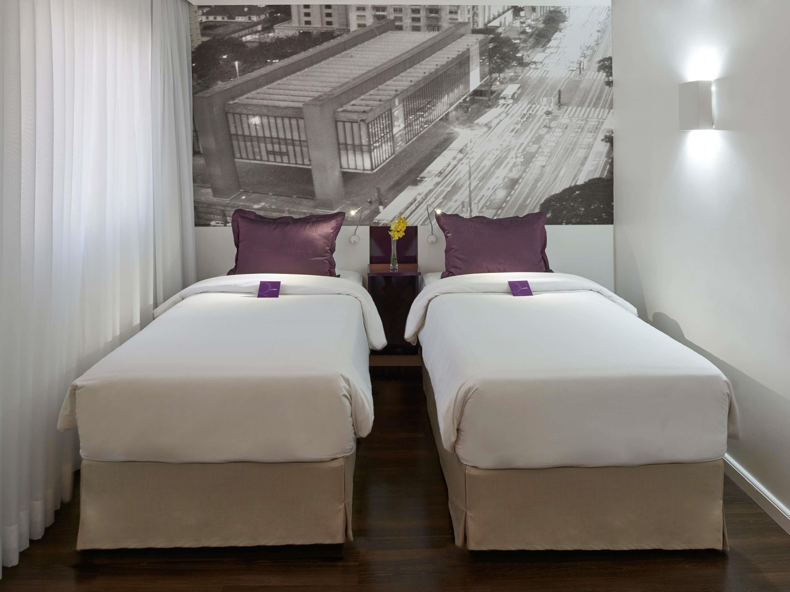 Ein Hotelzimmer mit zwei Betten, einer Stadtansicht-Mural an der Wand und Blick auf den Nachthimmel.