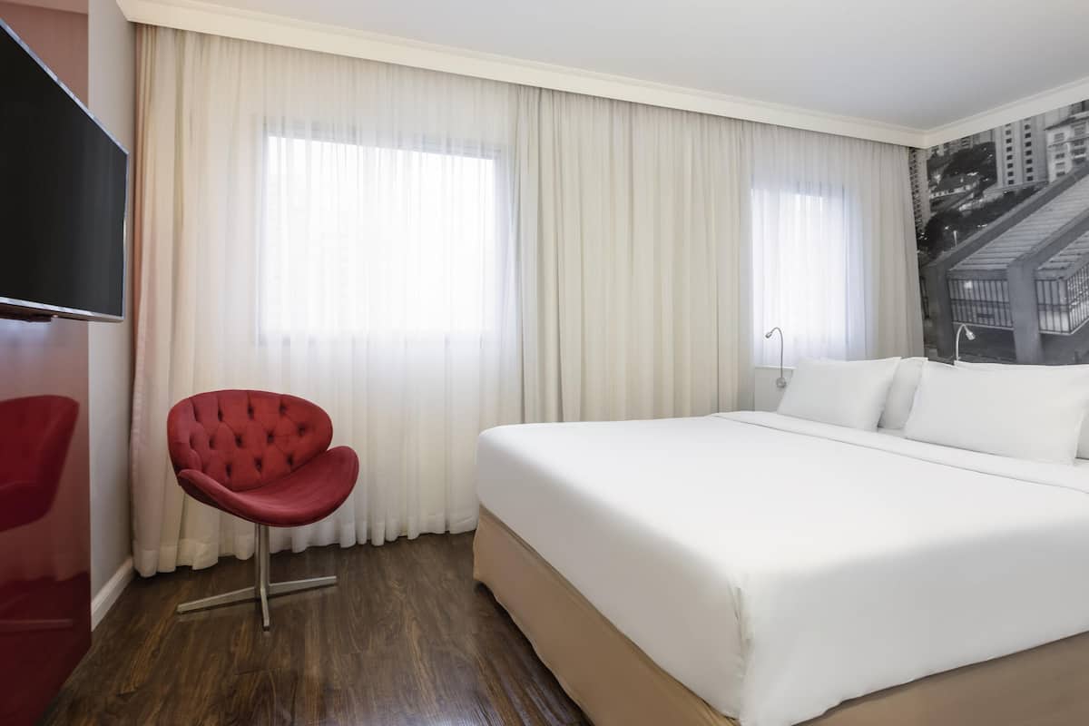 Una habitación de hotel con una cama grande, una silla roja y un televisor en la pared.
