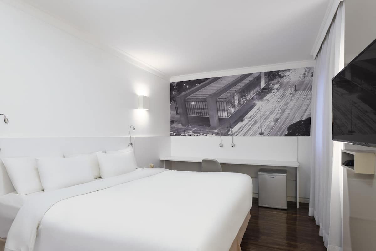 Una habitación de hotel moderna con una cama grande, un escritorio y un televisor de pantalla plana.