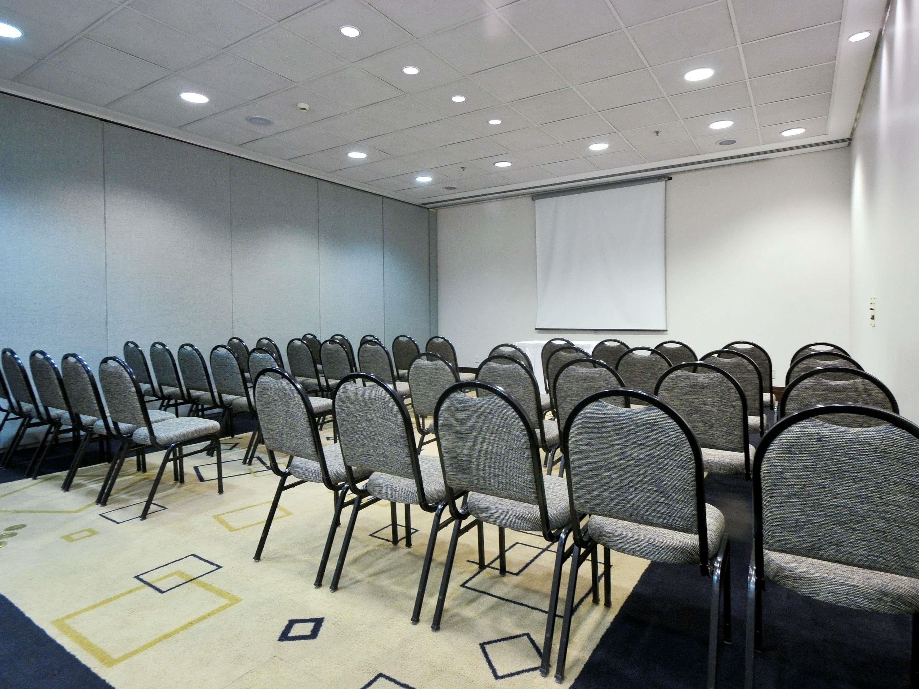 Una sala de conferències amb files de cadires, una pantalla de projector i un sòl amb moqueta.