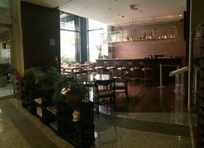 A restaurant with a brick wall, wooden tables, and chairs. There are potted plants and a fire feature.