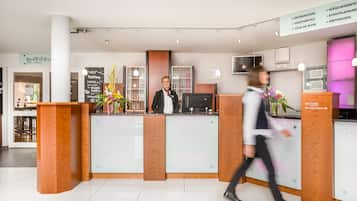 A hotel reception area with a modern design, featuring a reception desk, a digital screen, and a signboard with information.