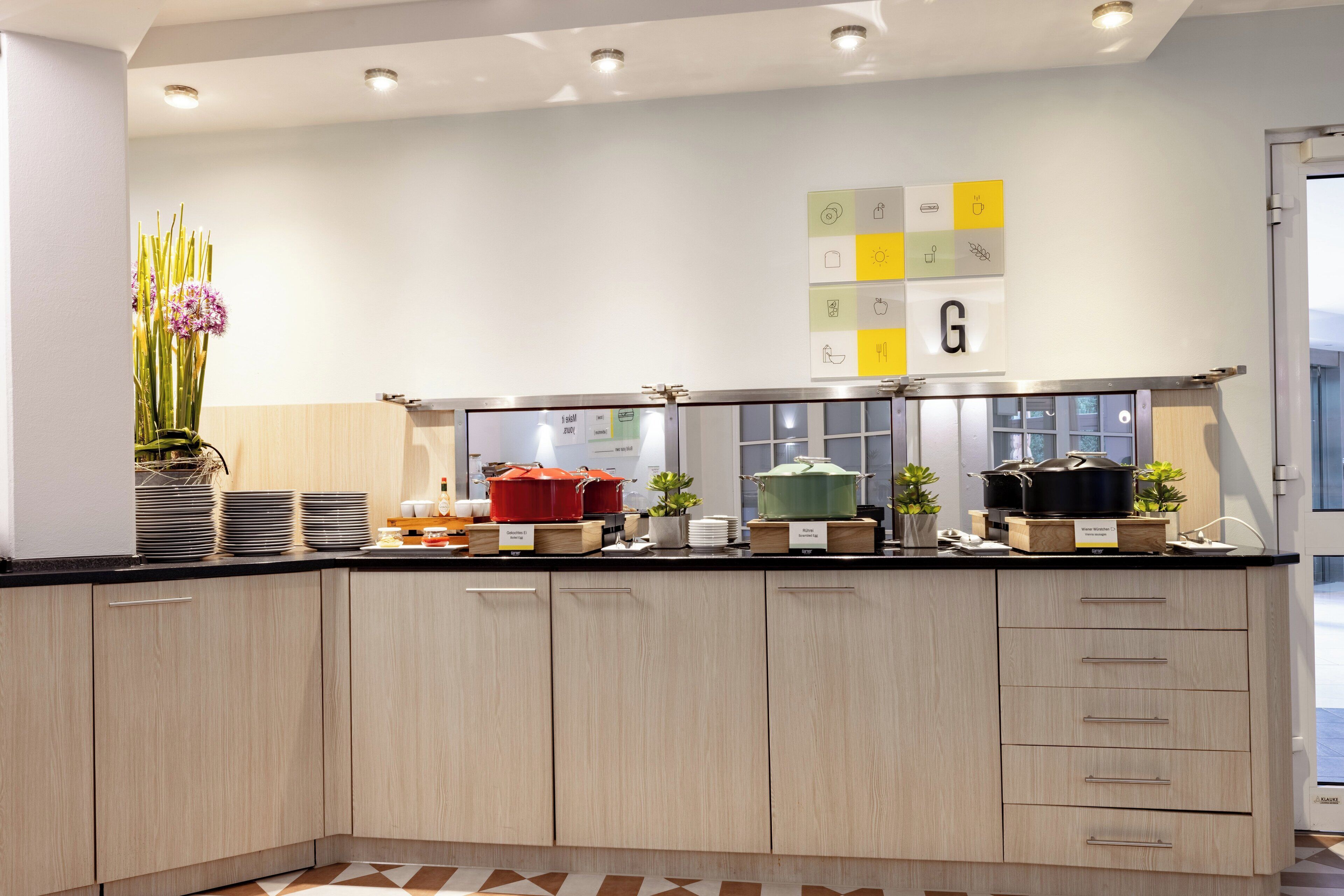 A modern kitchen with light wood cabinets, a black countertop, and various kitchen appliances.