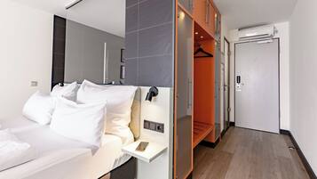 A modern hotel room with a bed, bedside table, and a walk-in closet with a mirror and hanging clothes.