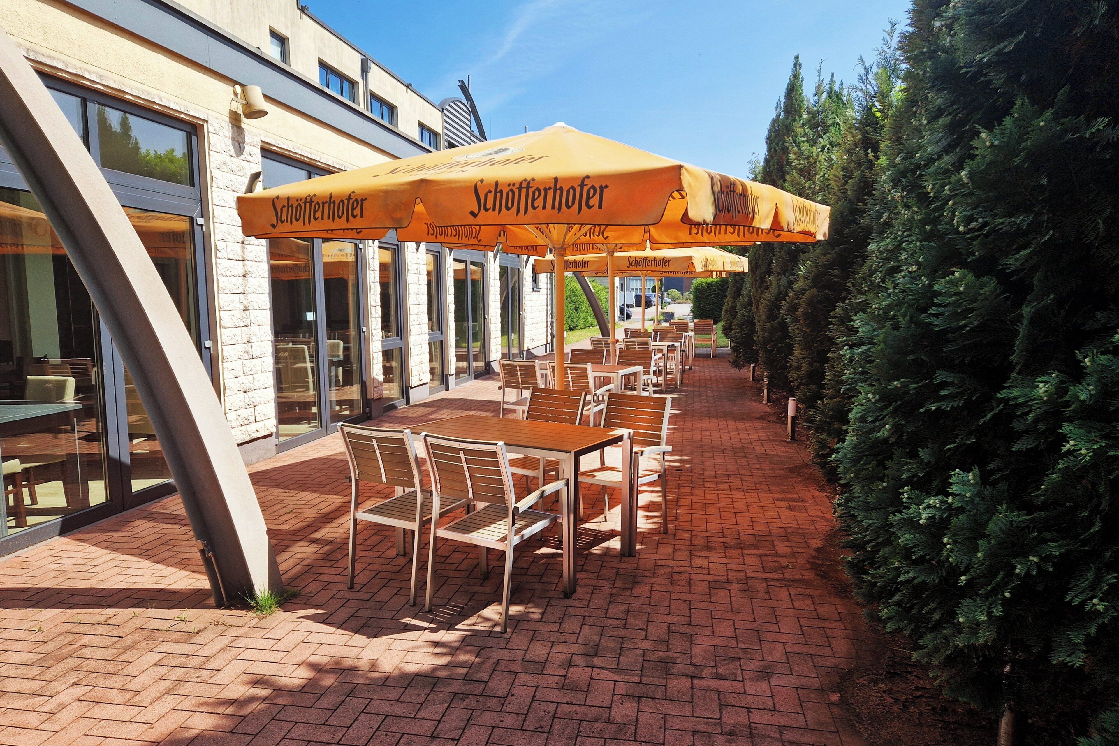 Un espace extérieur aménagé avec des tables et des chaises sous des parasols jaunes, un chemin en briques et un bâtiment doté de grandes fenêtres.