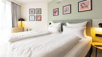 A hotel room with two beds, a desk, a chair, and a lamp. There are framed pictures on the wall.