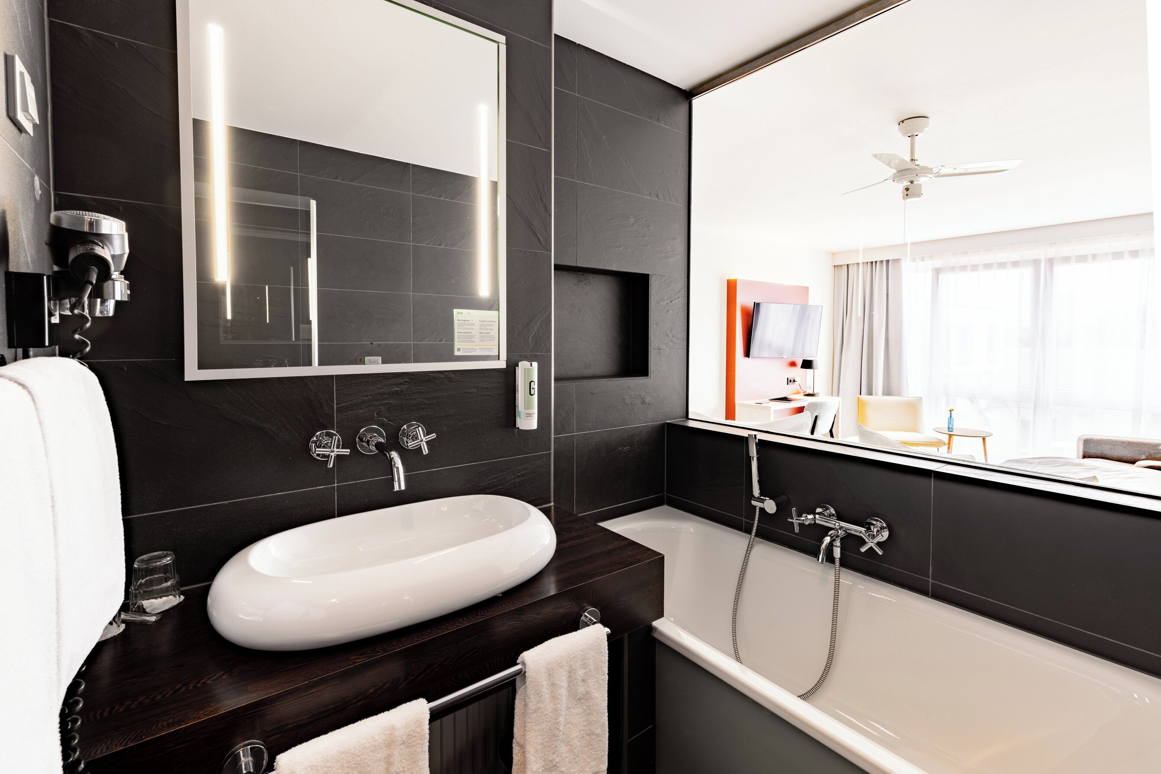 Un baño moderno con un lavamanos ovalado grande, una bañera y un ventilador de techo.