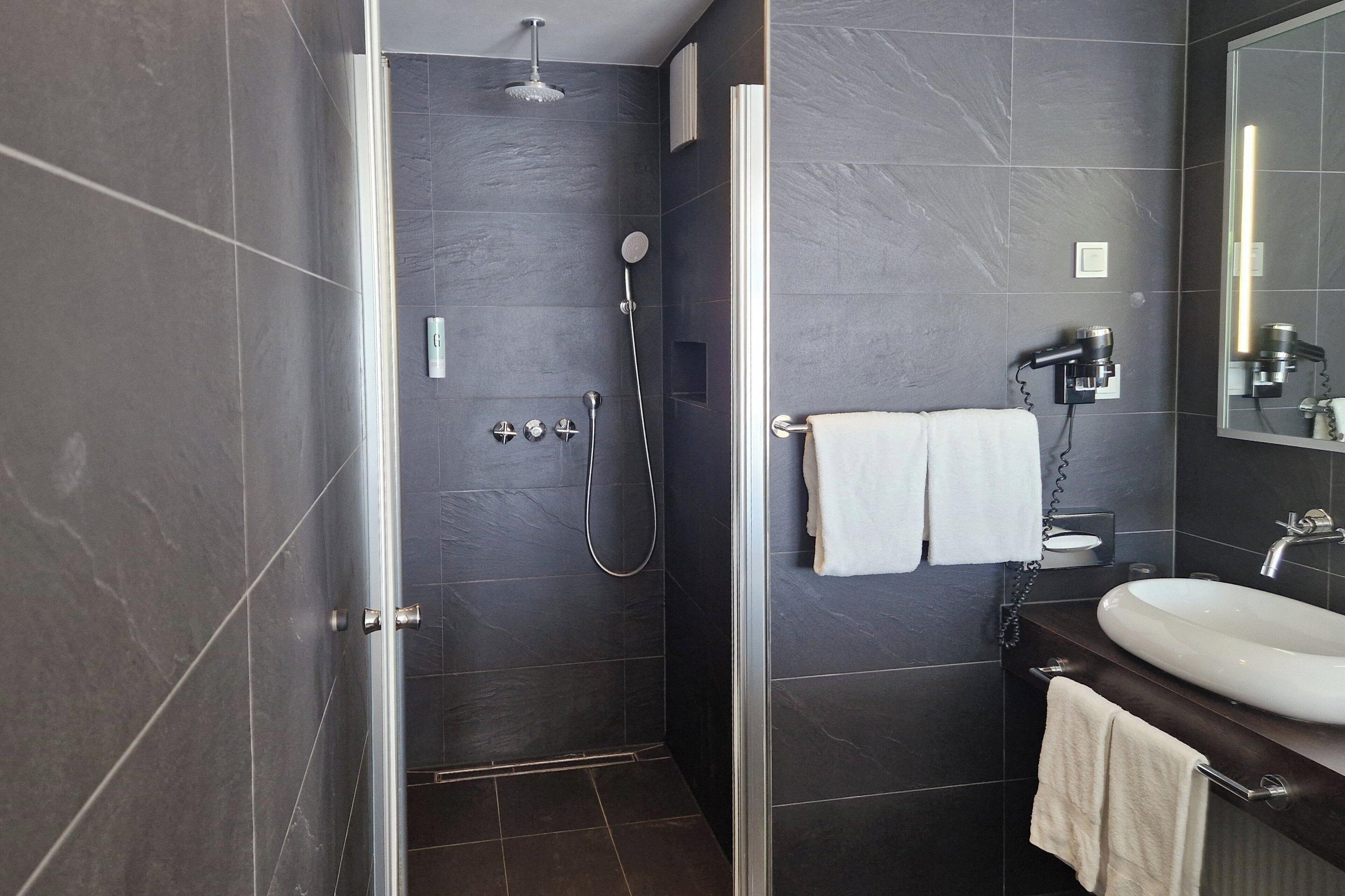 A modern bathroom with a glass-enclosed shower, a white sink, and a large mirror.