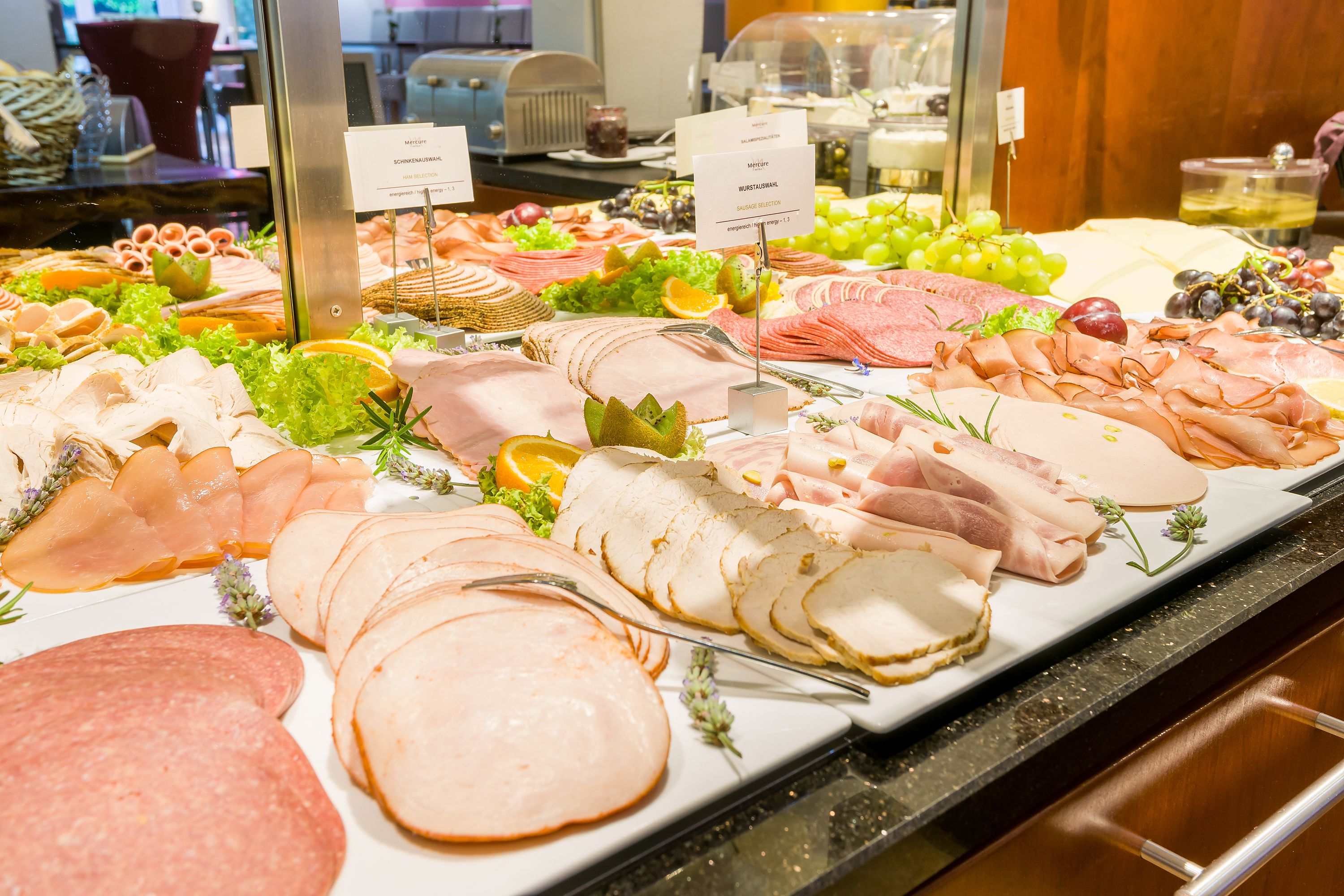 Ett urval av olika sorters pålägg och ostar, upplagt på ett buffébord, med etiketter som anger de olika typerna.