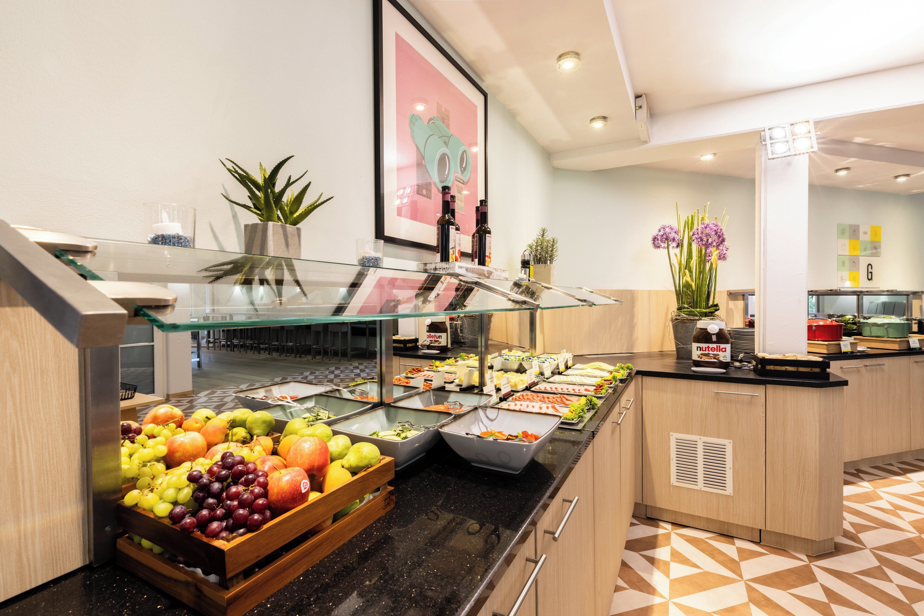 A buffet with various fruits and beverages, a potted plant, and a framed picture on the wall.