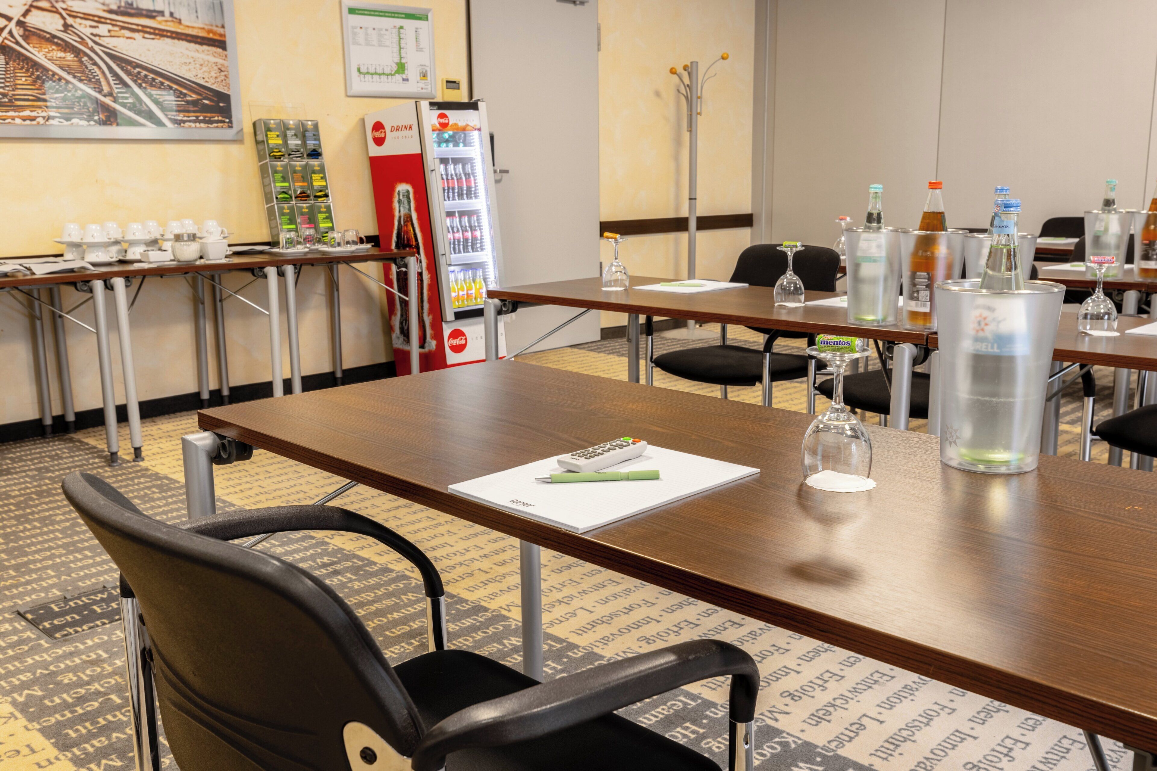 A conference room with tables, chairs, a refrigerator, and a Coca-Cola vending machine.