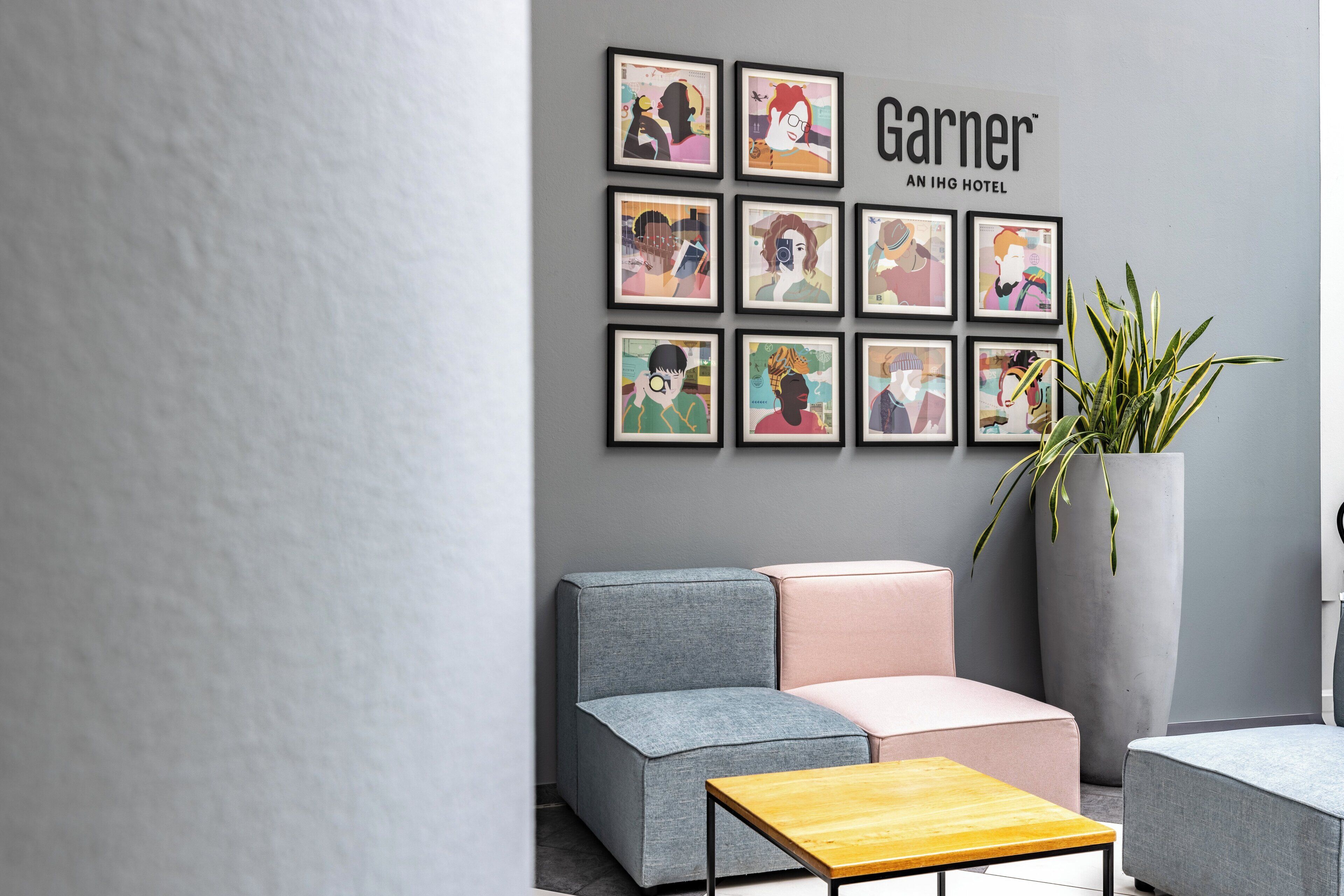 A modern hotel lobby with a grey wall, a large potted plant, and a seating area with grey and pink sofas.