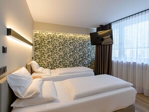 A hotel room with two beds, a TV mounted on the wall, and a window with curtains. - Mercure Hotel München Altstadt (Munich)