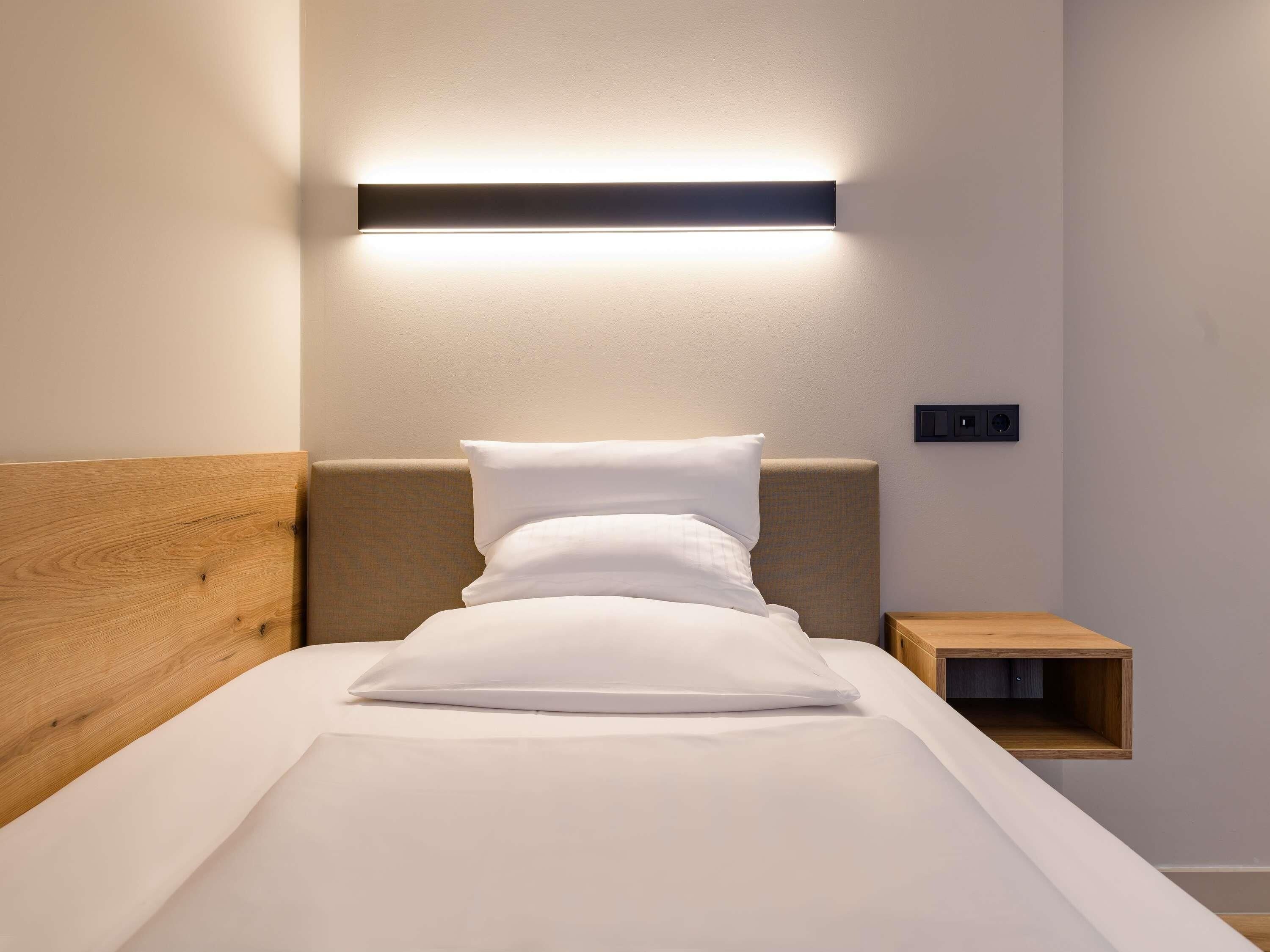 A neatly made bed with a wooden headboard, a bedside table, and a wall-mounted light fixture.