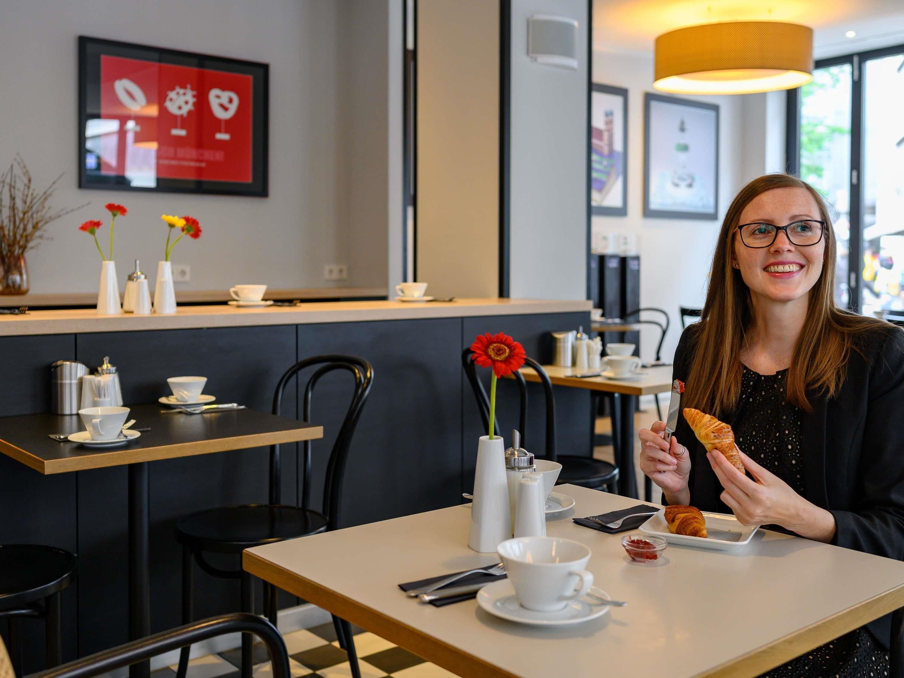 Un interior de cafetería con mesas, sillas y una pizarra con el menú.
