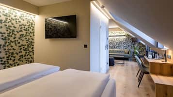 Un dormitorio con dos camas, un televisor, un escritorio con silla, y una escalera que lleva a una sala de estar con sofá y cafetera.