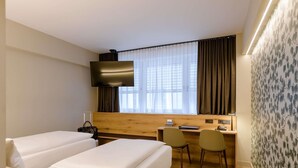 A hotel room with two beds, a desk, two chairs, a TV, and a window with curtains. - Mercure Hotel München Altstadt (Munich)