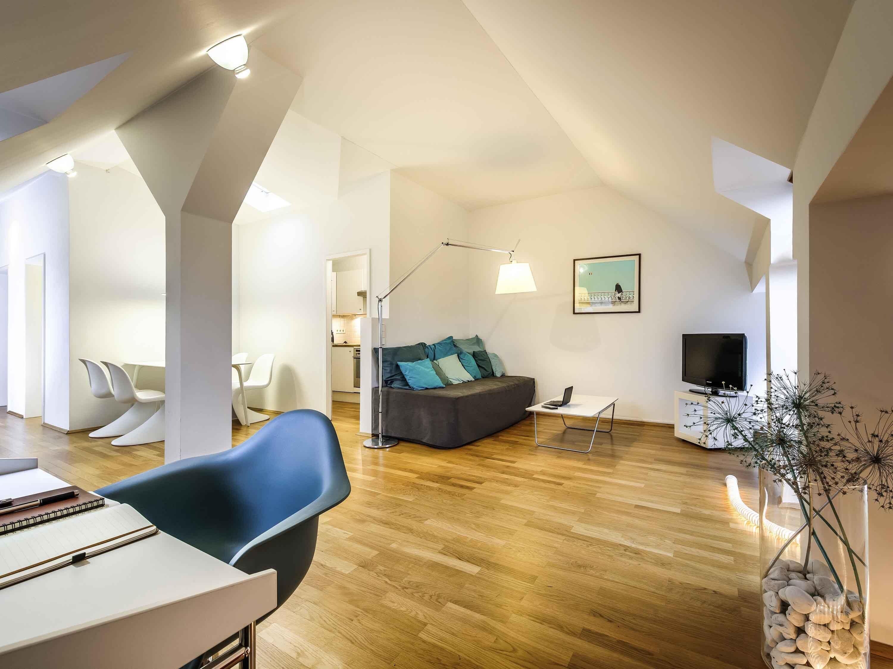 Ein modernes Wohnzimmer mit einer Couch, einem Essbereich mit Stühlen, einem Fernseher und einer Lampe.