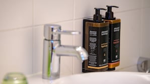 A bathroom with a white sink, a modern faucet, and two Elemental Herbology body wash bottles. - Mercure Hotel München Altstadt (Munich)