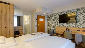 A hotel room with a large bed, a desk, a chair, a TV, and a wardrobe.