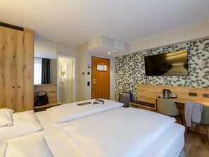 A hotel room with a large bed, a desk, a chair, a TV, and a wardrobe. - Mercure Hotel München Altstadt (Munich)