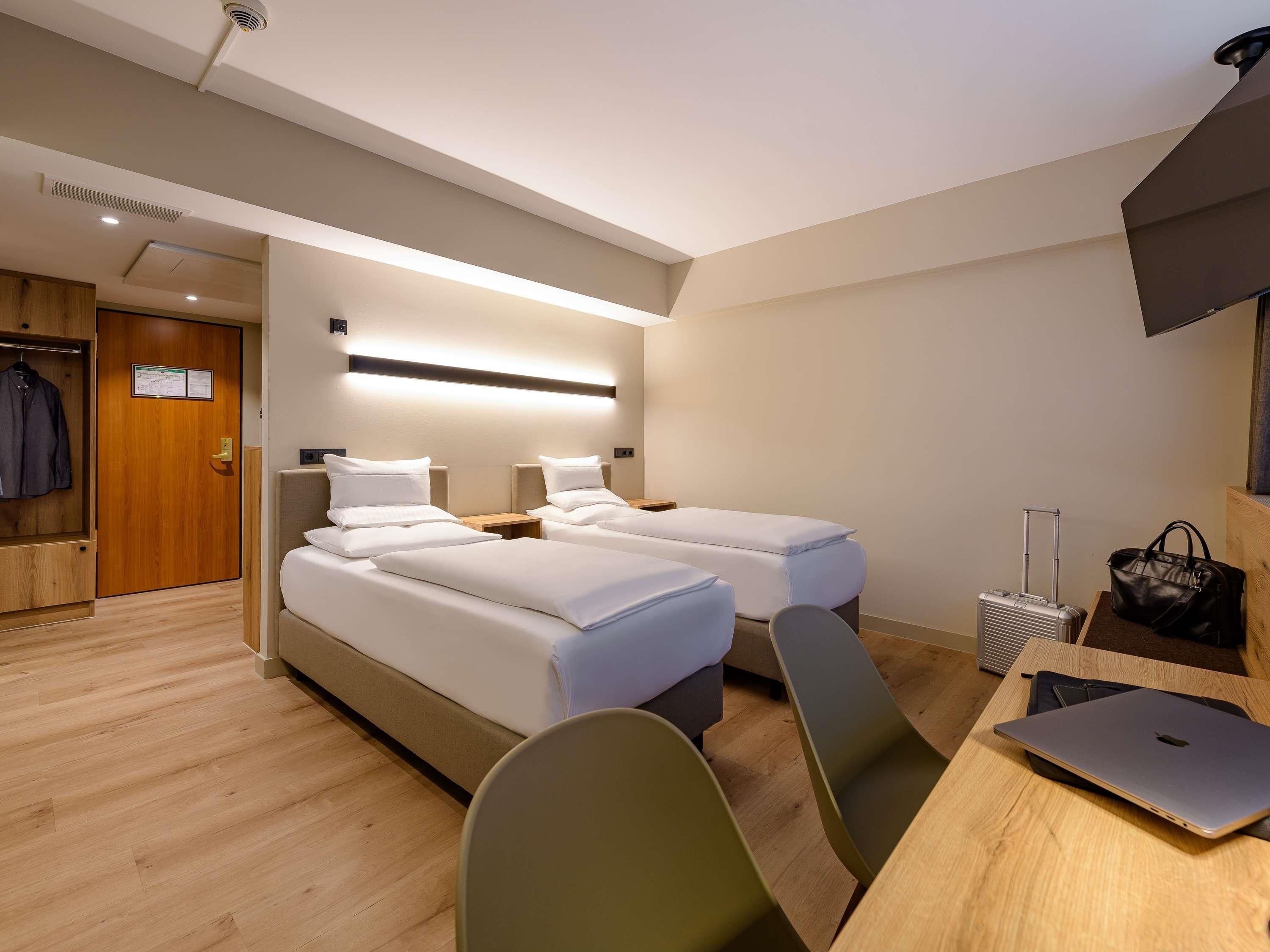 Een hotelkamer met twee bedden, een bureau met een laptop, een stoel, een koffer en een kapstok.