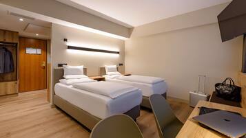 Een hotelkamer met twee bedden, een bureau met een laptop, een stoel, een koffer en een kapstok.