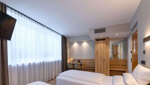 Habitació d'hotel amb dos llits, una taula de nit, una cadira, un mirall i una finestra amb cortines.