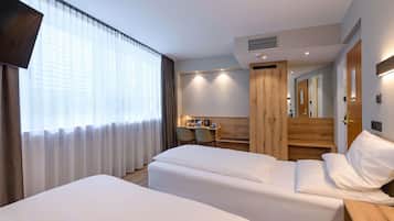 Habitación de hotel con dos camas, un escritorio, una silla, un espejo y una ventana con cortinas.