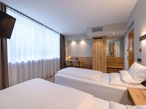 A hotel room with two beds, a desk, a chair, a mirror, and a window with curtains. - Mercure Hotel München Altstadt (Munich)