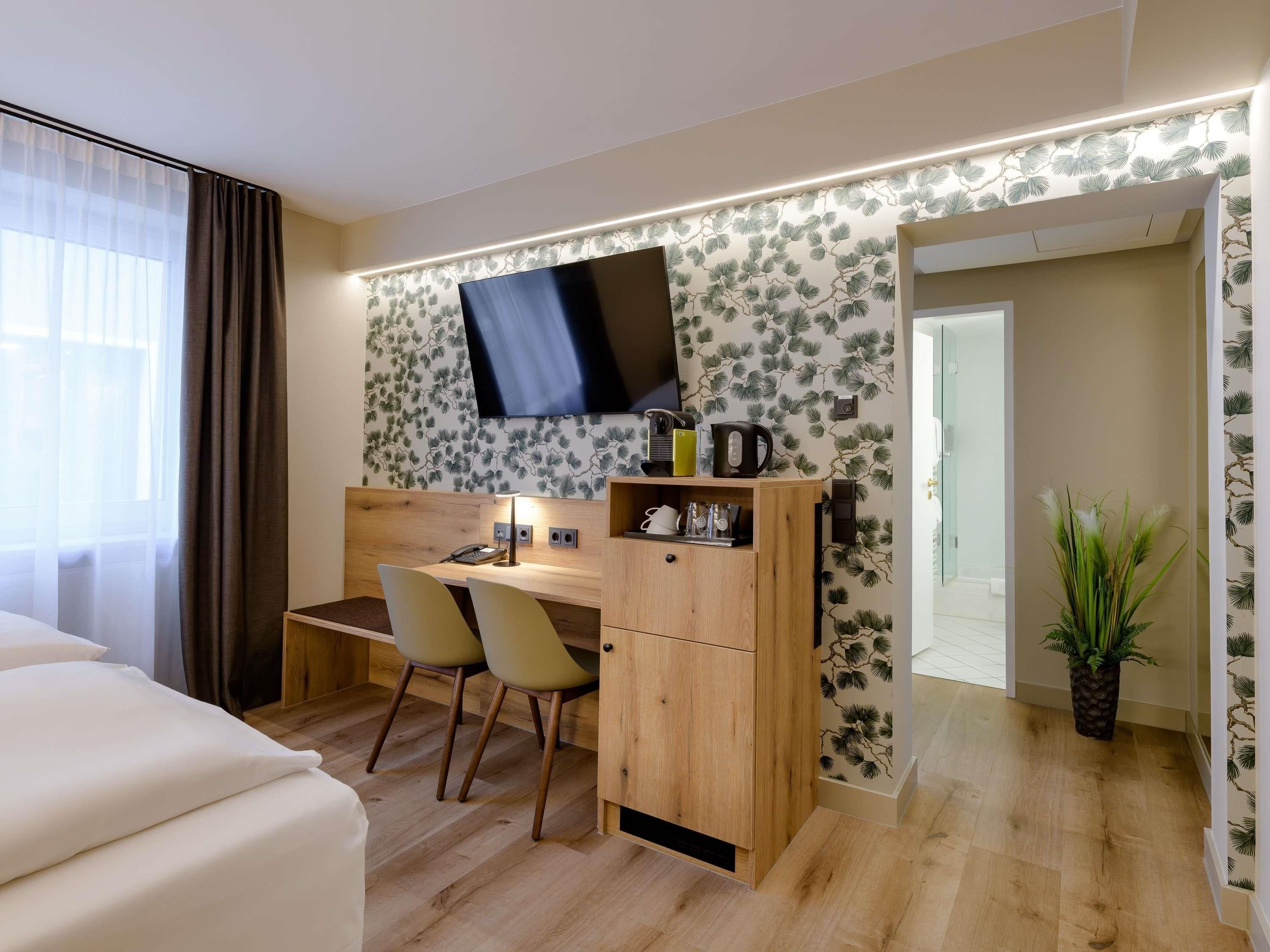 A compact hotel room with a desk, chair, and a television mounted on the wall.