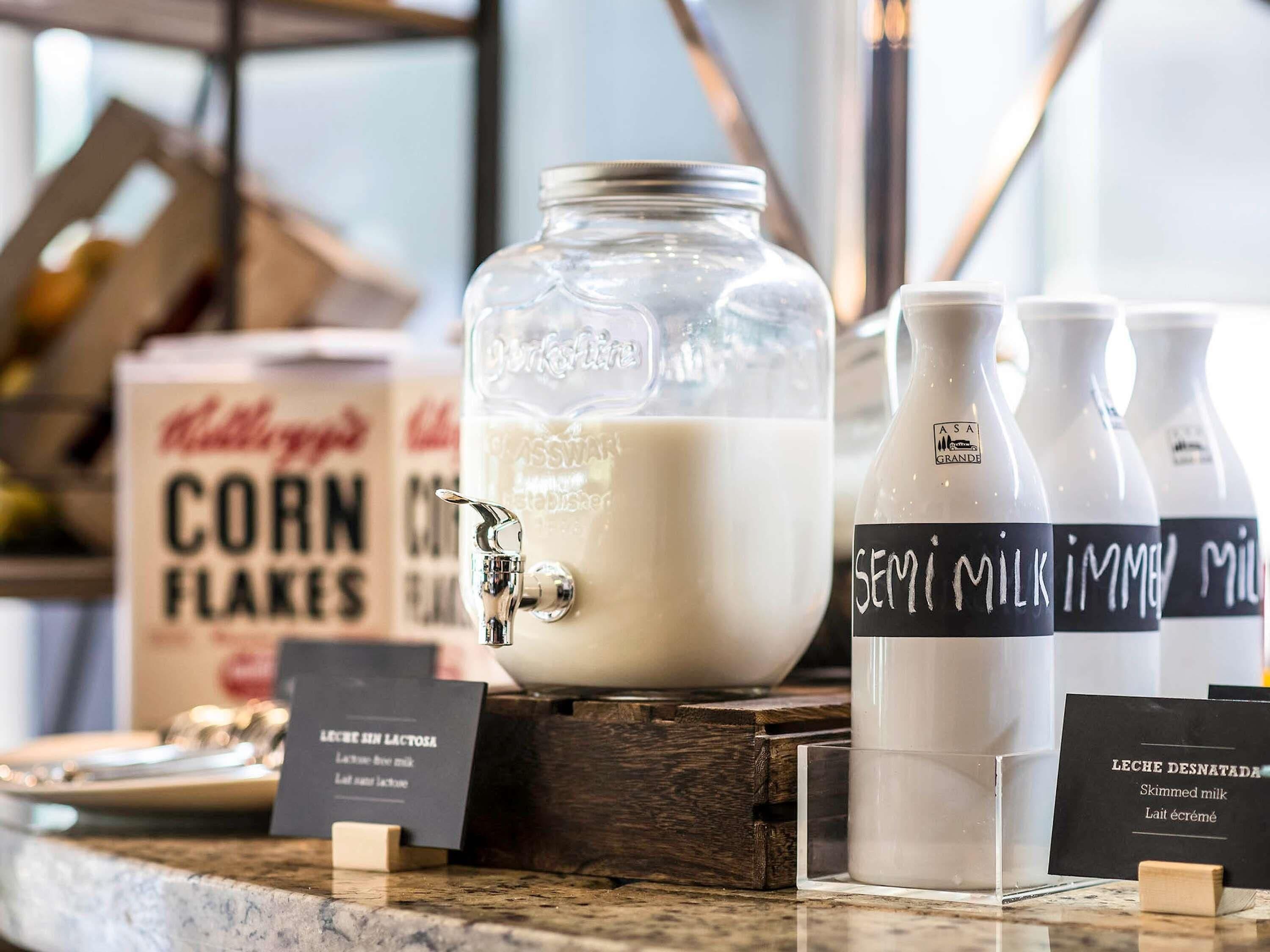 A milk station with a large glass jar, bottles labeled 'SEMI MILK,' and a box of 'CORN FLOKES.'