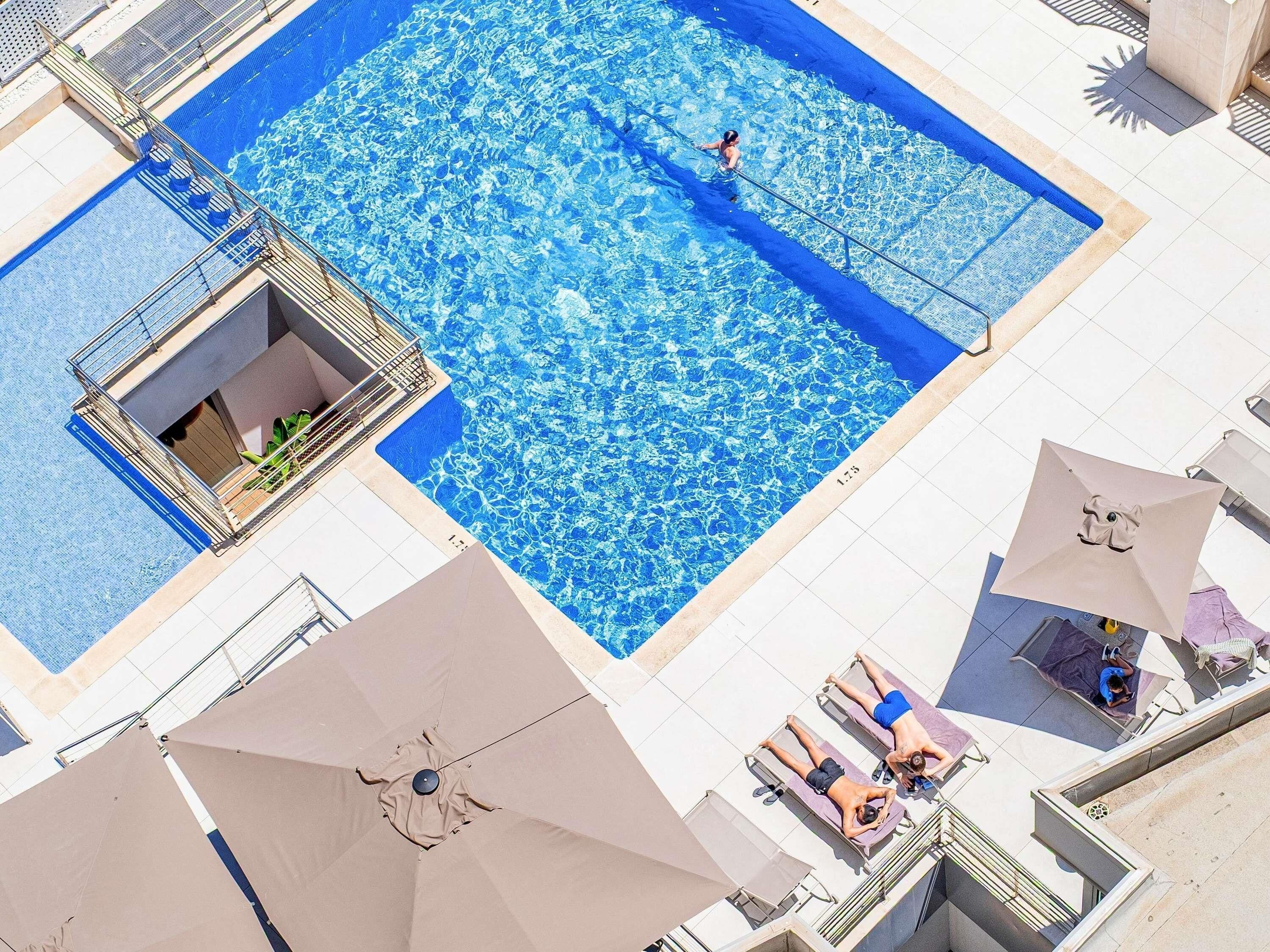 A rooftop swimming pool with a diving board, lounge chairs, and umbrellas.