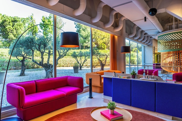 Un interior moderno con un sofá rojo, una zona de cocina azul y grandes ventanas con vistas a árboles y follaje.
