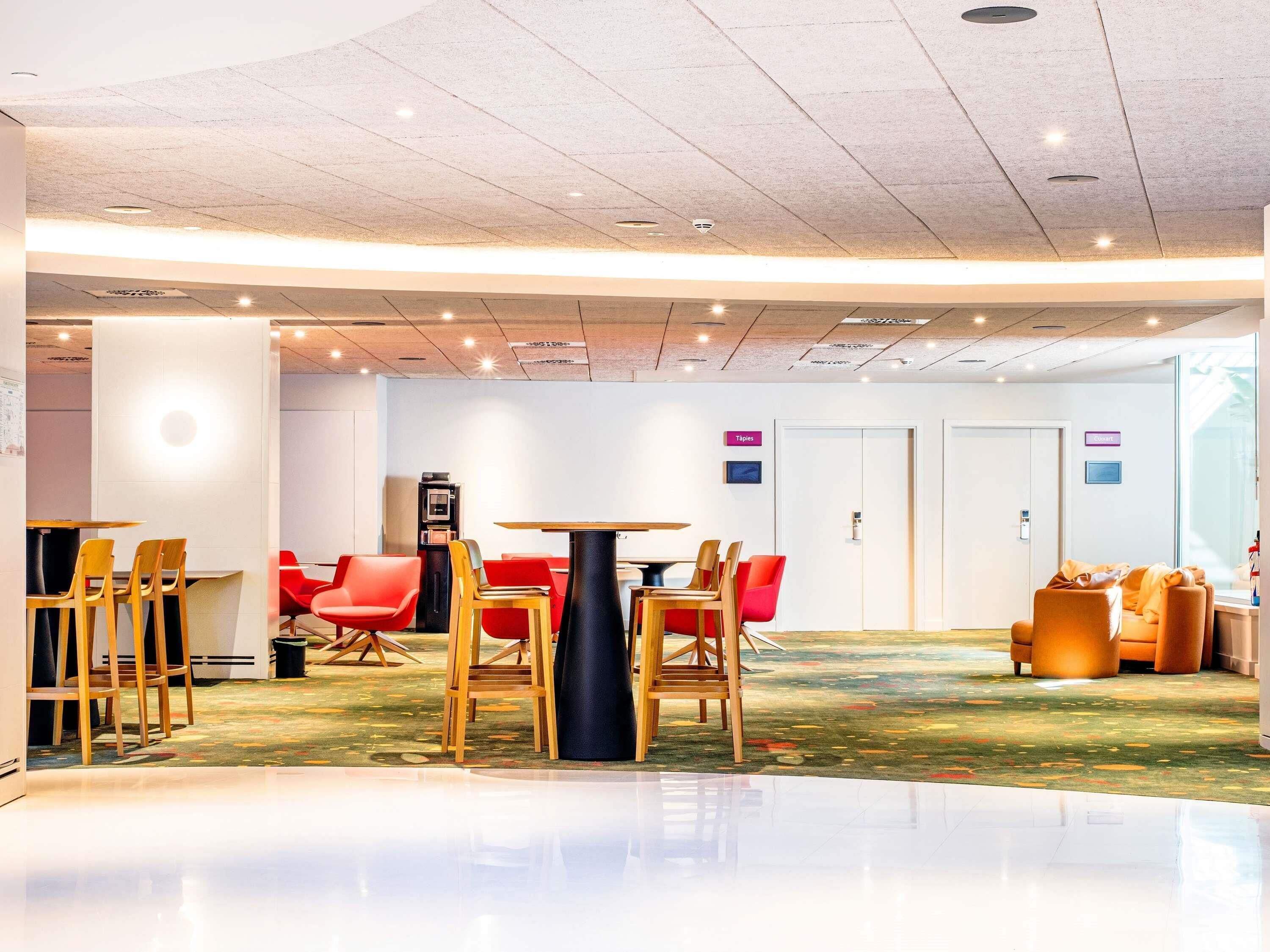 Un moderno vestíbulo de hotel con un área de estar central, una máquina de café y una recepción.