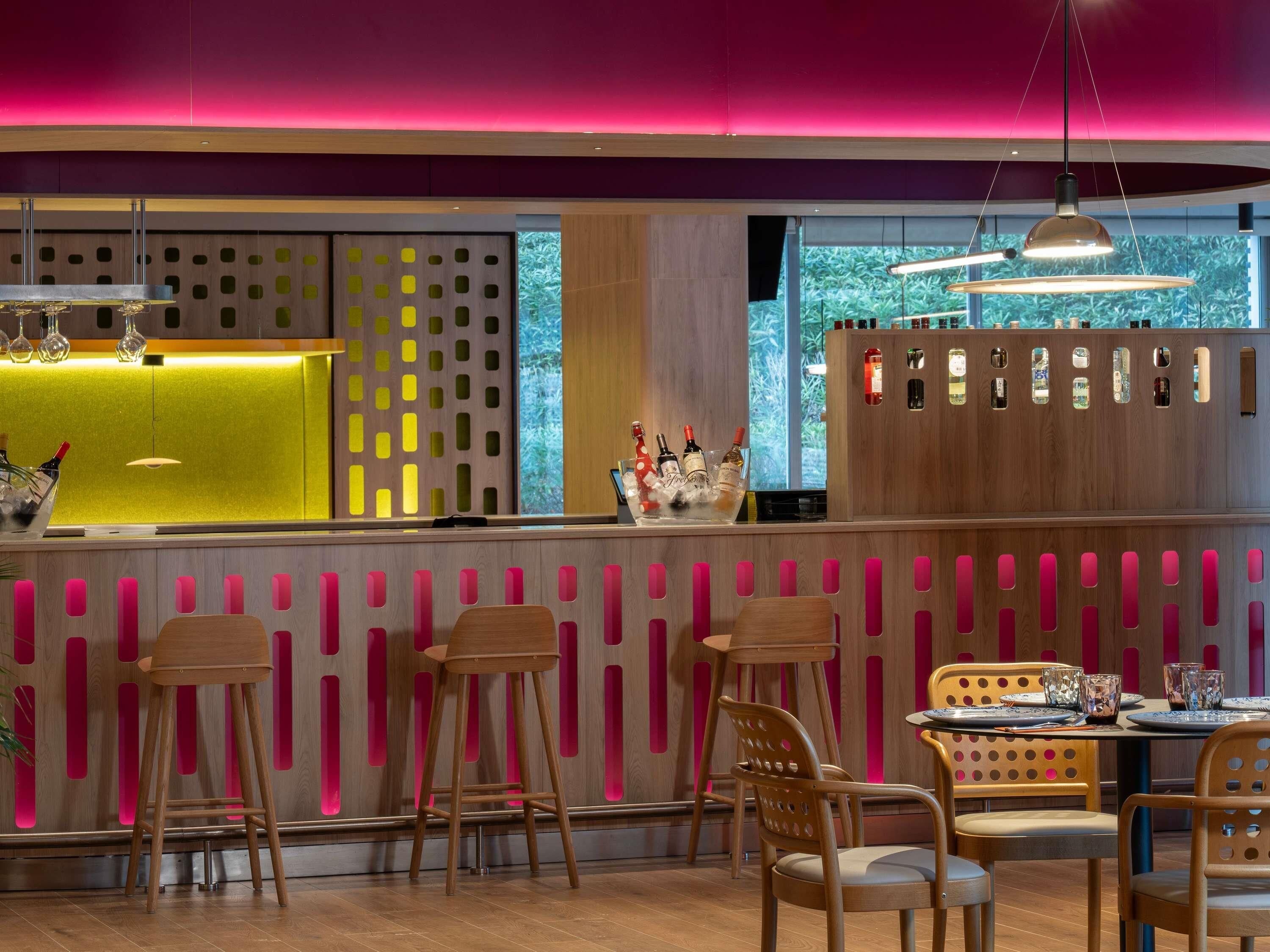 A modern bar area with wooden furniture, a bar counter, and a view of greenery outside.