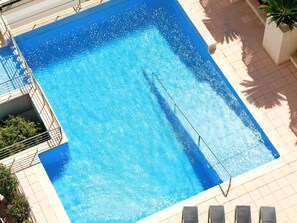 A rectangular swimming pool with a clear blue water surface, surrounded by a tiled deck and a metal pool ladder.